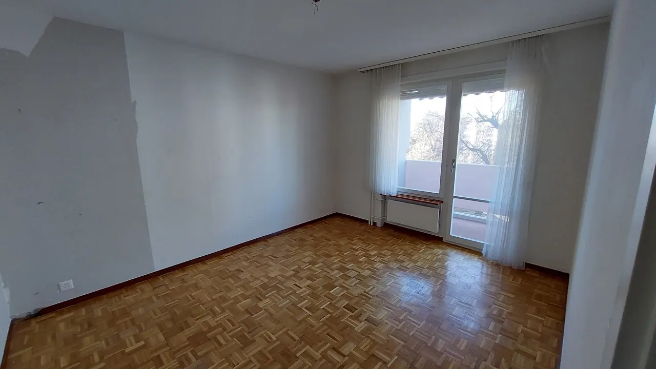 Pièce de vie vide avec parquet mosaïque avant rénovation d'appartement à Fribourg.