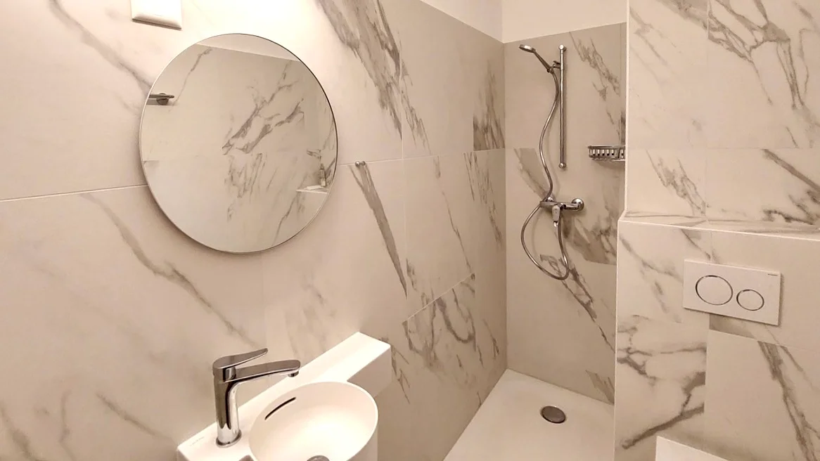 Salle de bain moderne avec carrelage effet marbre et miroir rond à Fribourg.